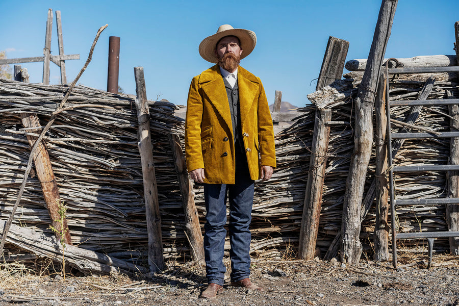 Model wearing Men's Gold Corduroy Jacket paired with grey herringbone vest, blue rugged Levis jeans, and a beige cowboy hat